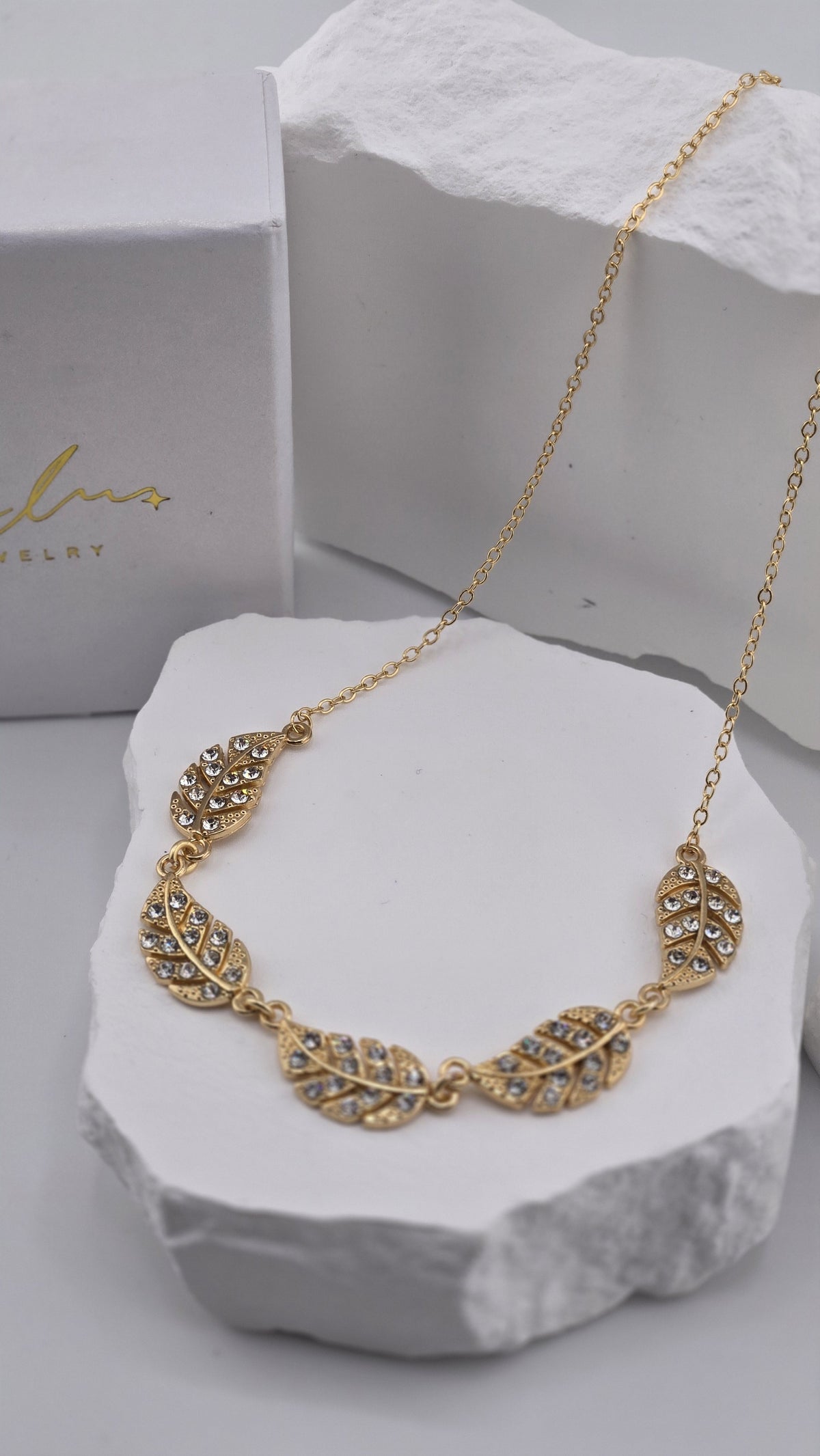 Close-up of the Feather Garland Necklace showing five gold-plated feathers with clear stones