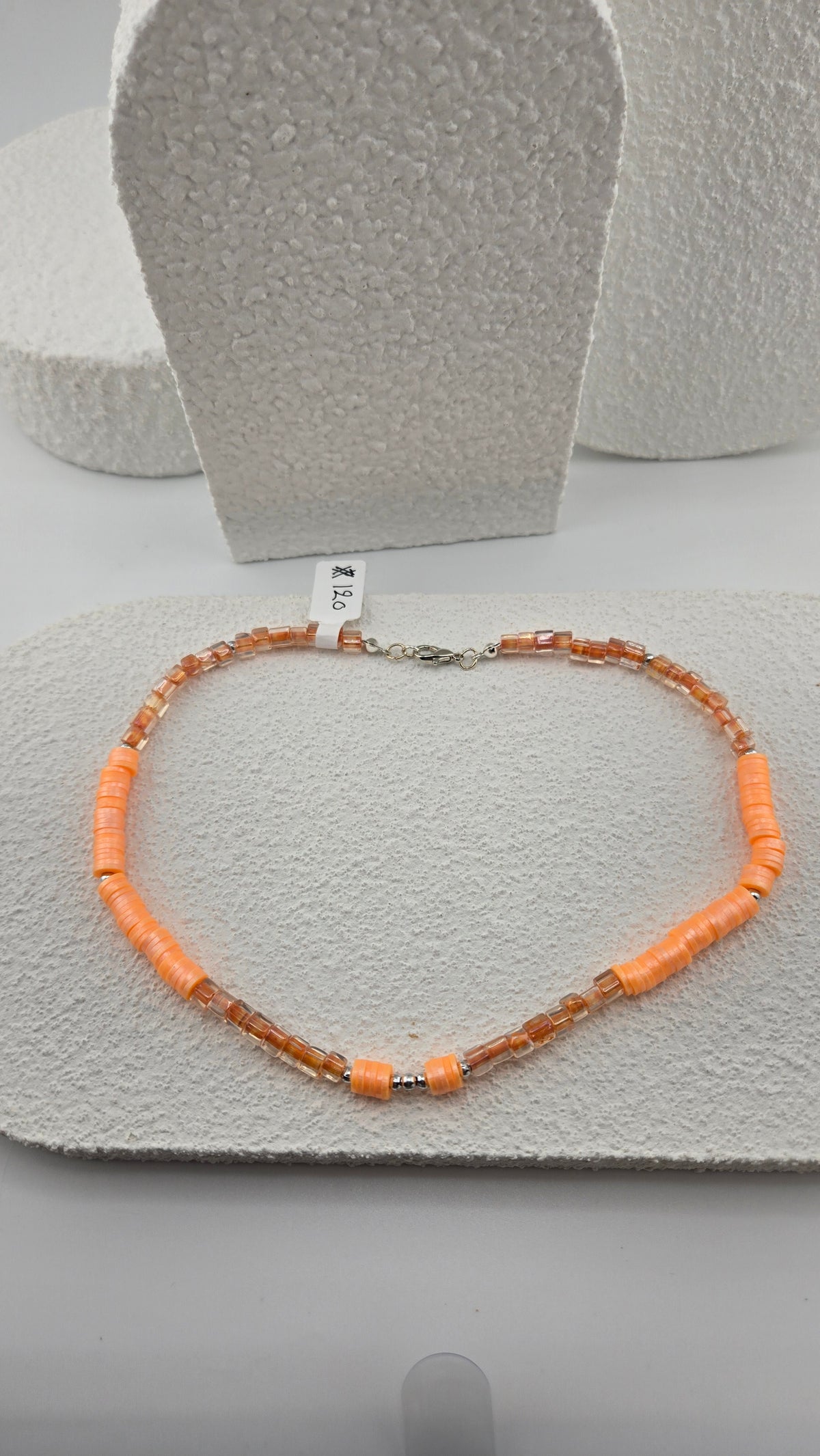 Apricot Glow Necklace laid in a heart shape on a white textured stand, with apricot-orange disc beads, clear amber glass beads and small silver-tone spacers