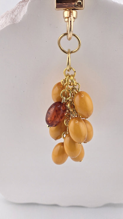 Butterscotch Bag Charm hanging from its gold-tone clip, butterscotch-colored beads with one darker amber-colored bead