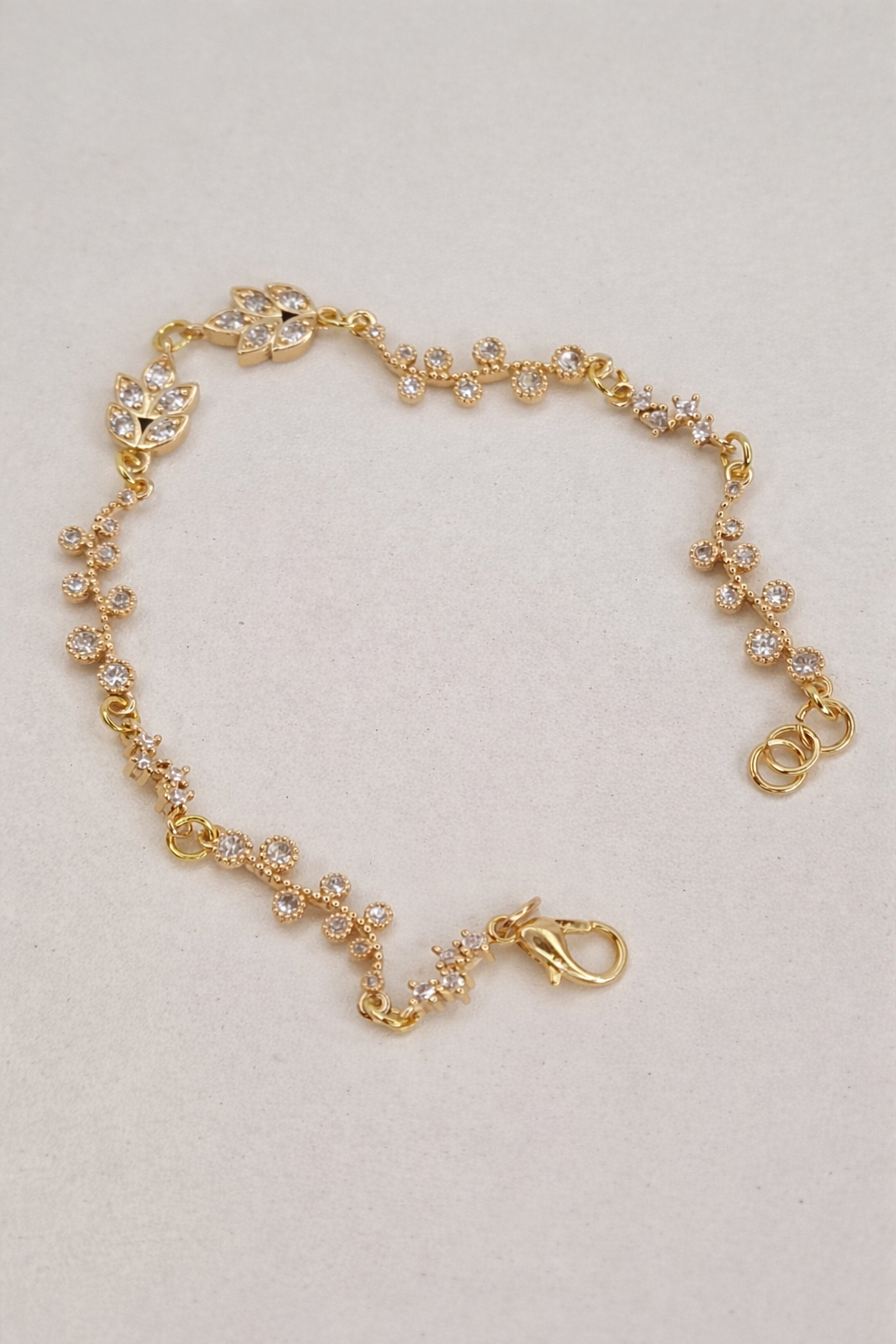 Woman's hand wearing the Golden Flora Bracelet, holding a bouquet of flowers, representing nature-inspired elegance.
