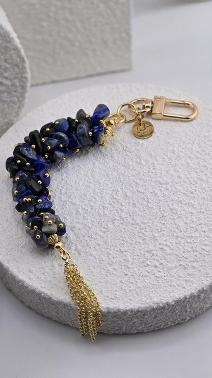 Indigo Tassel Bag Charm, a cluster of deep blue, black and gray natural stone chips with gold beads, a gold-plated chain tassel and a round LuluTouch charm
