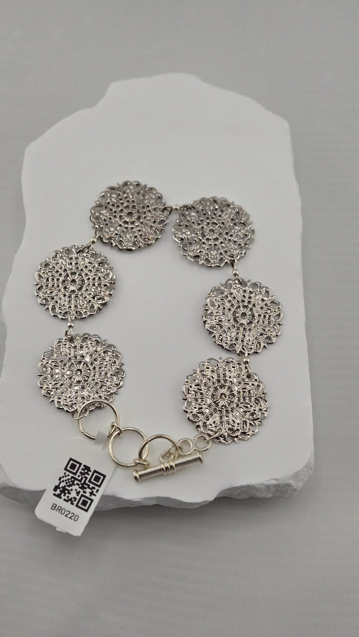 Silver-tone lace-like medallions linked into a bracelet on a white stone