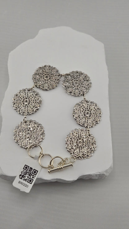 Silver-tone lace-like medallions linked into a bracelet on a white stone