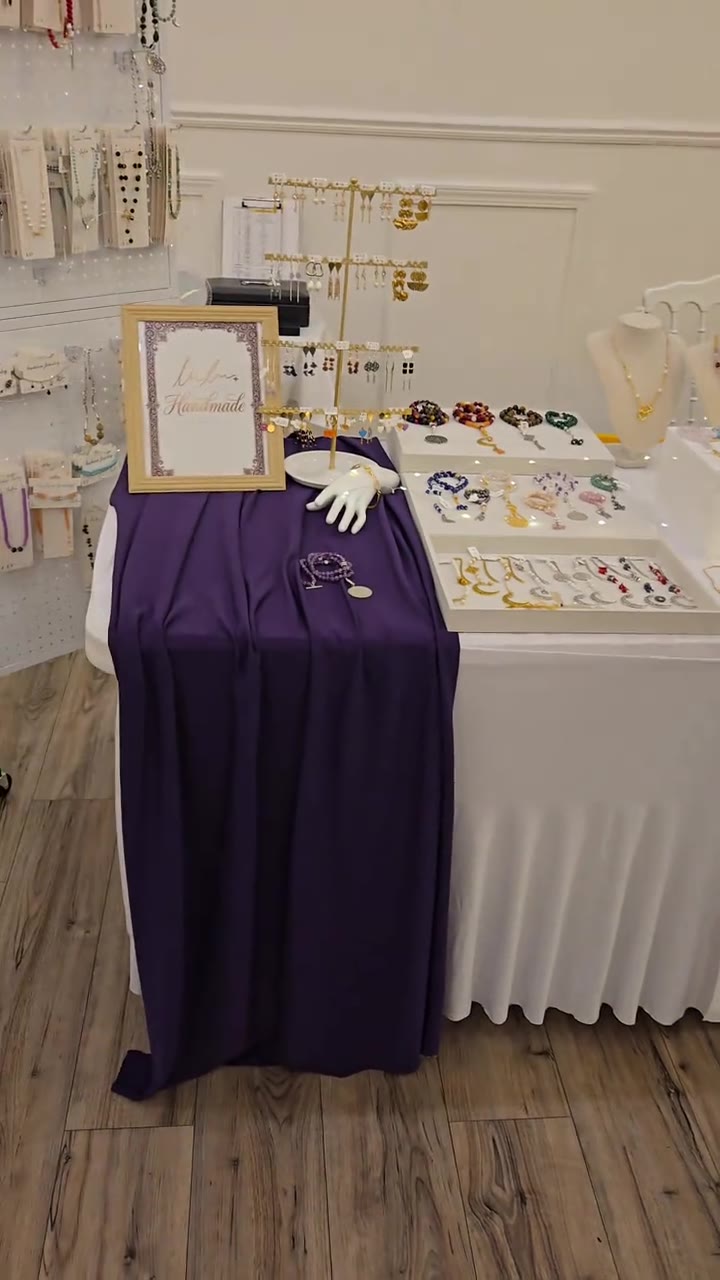 Her bazaar table with a purple runner, a Handmade sign, necklaces and tasbih trays