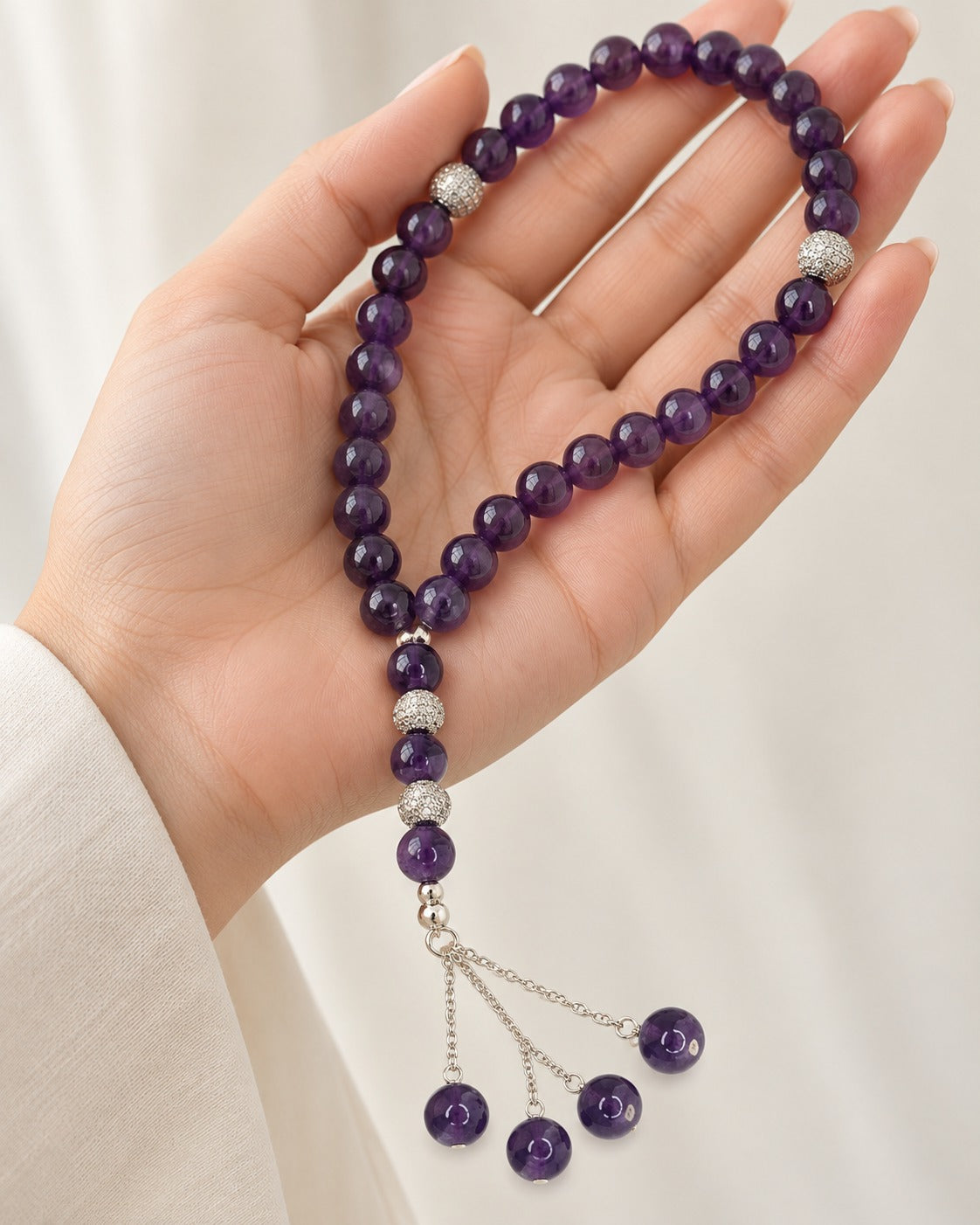Royal Amethyst Tasbih held in an open hand, showing deep purple amethyst beads, silver pavé accents and a chain tassel with four amethyst drops