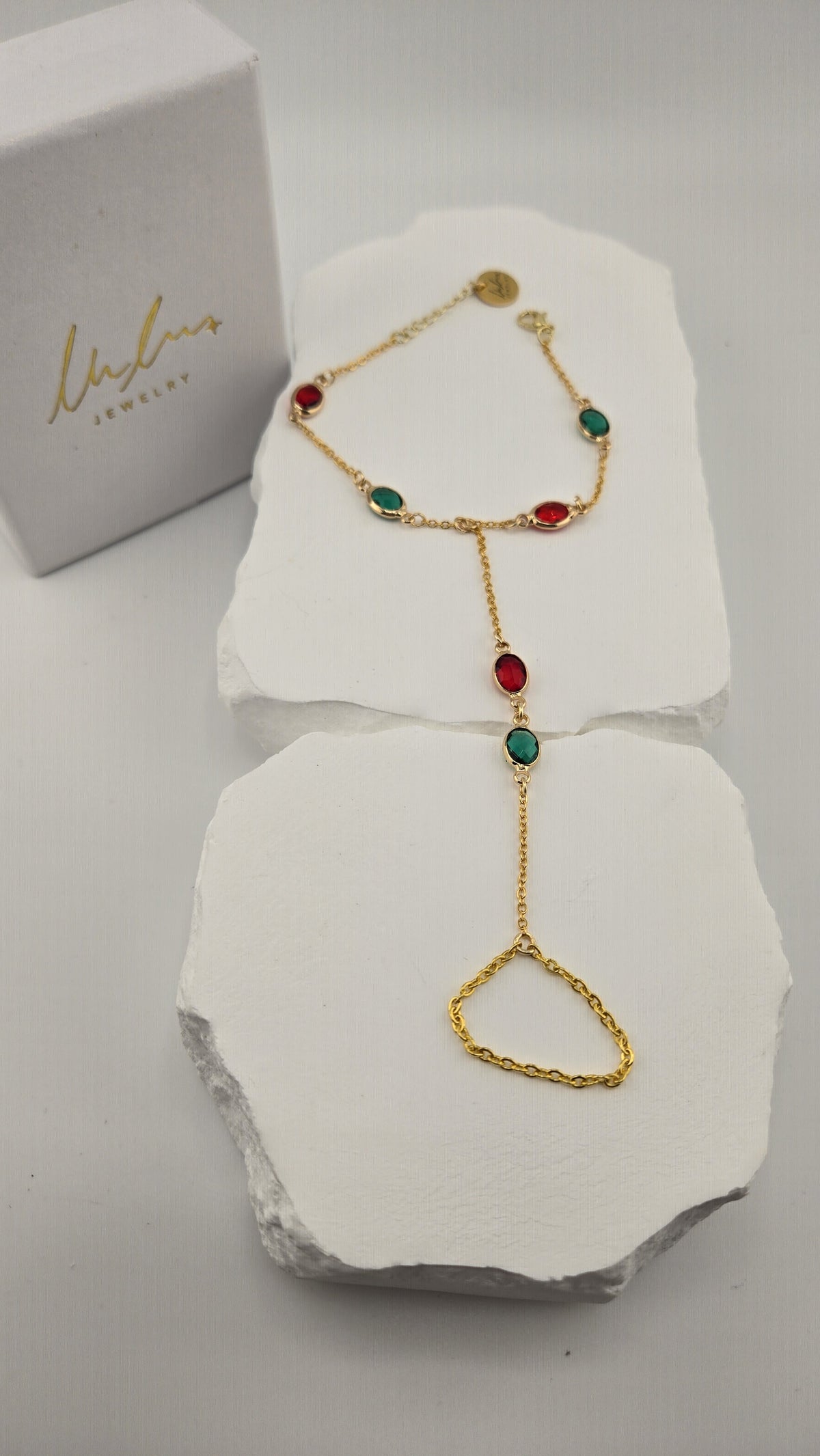 Sultana Hand Chain with red and green oval stones beside the LuluTouch box